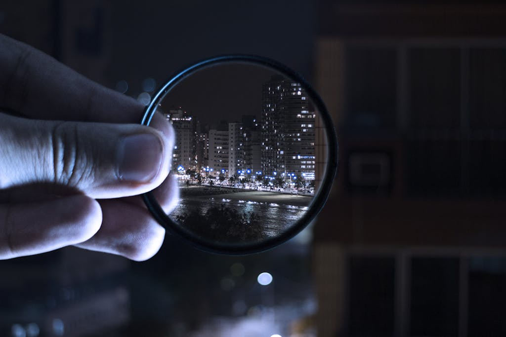 A hand holding a lens filter enhances a vibrant city nightlife scene.